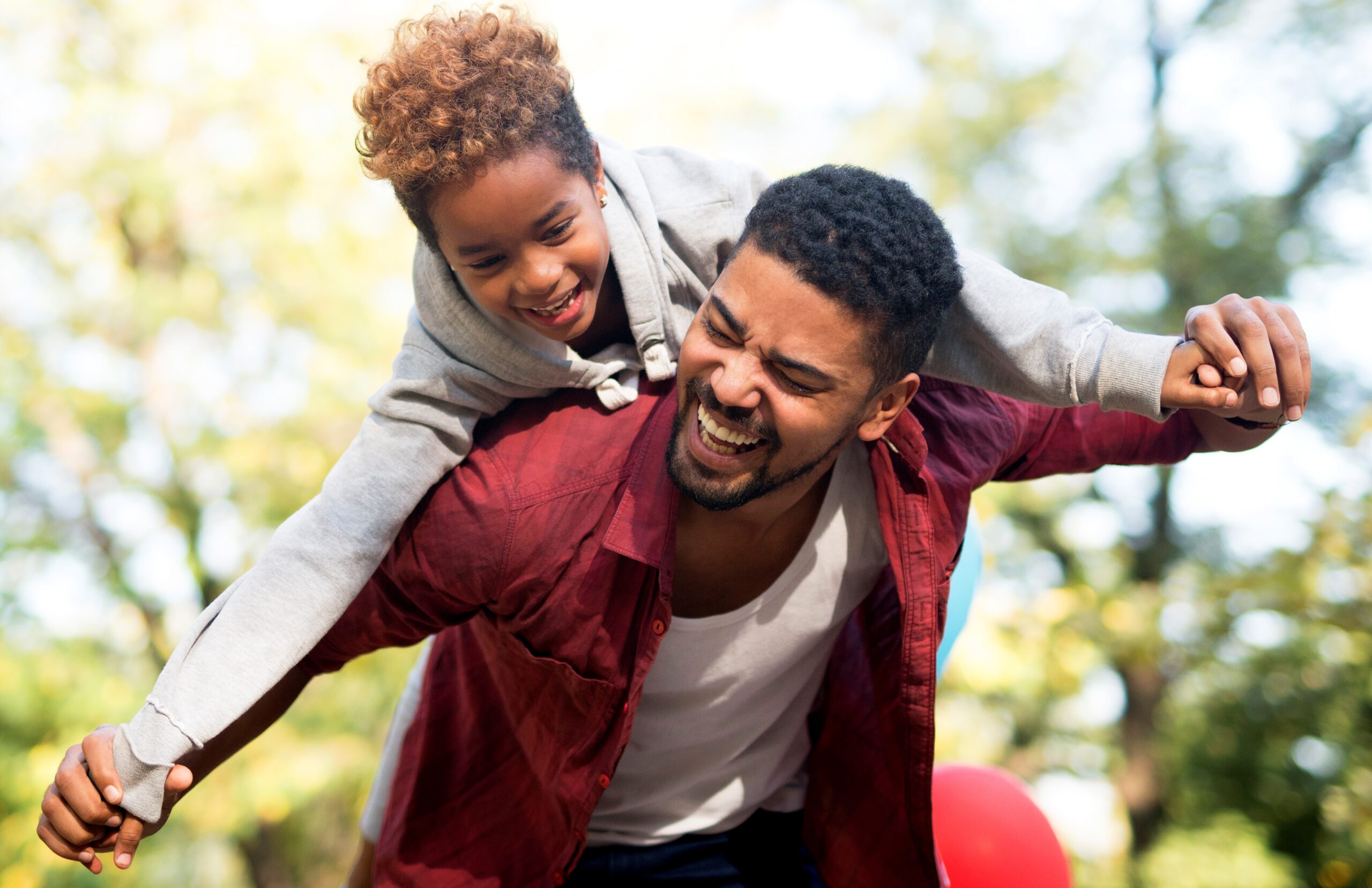 Father carrying daughter on his back with arms spread.